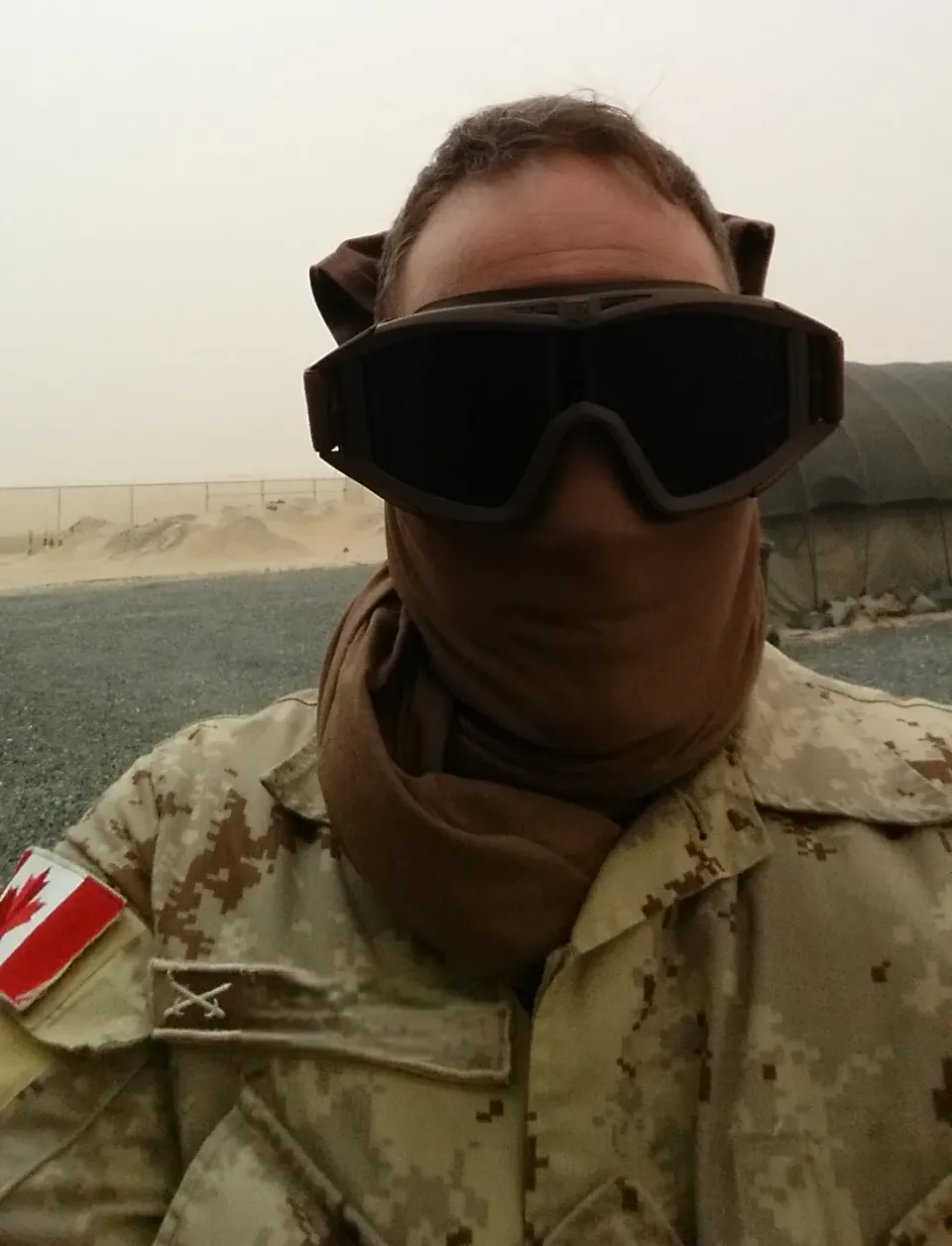 A real picture of Joe standing in a desert, face & eyes covered in military sand-goggles, deployed on operations with the CAF circa 2014/15.