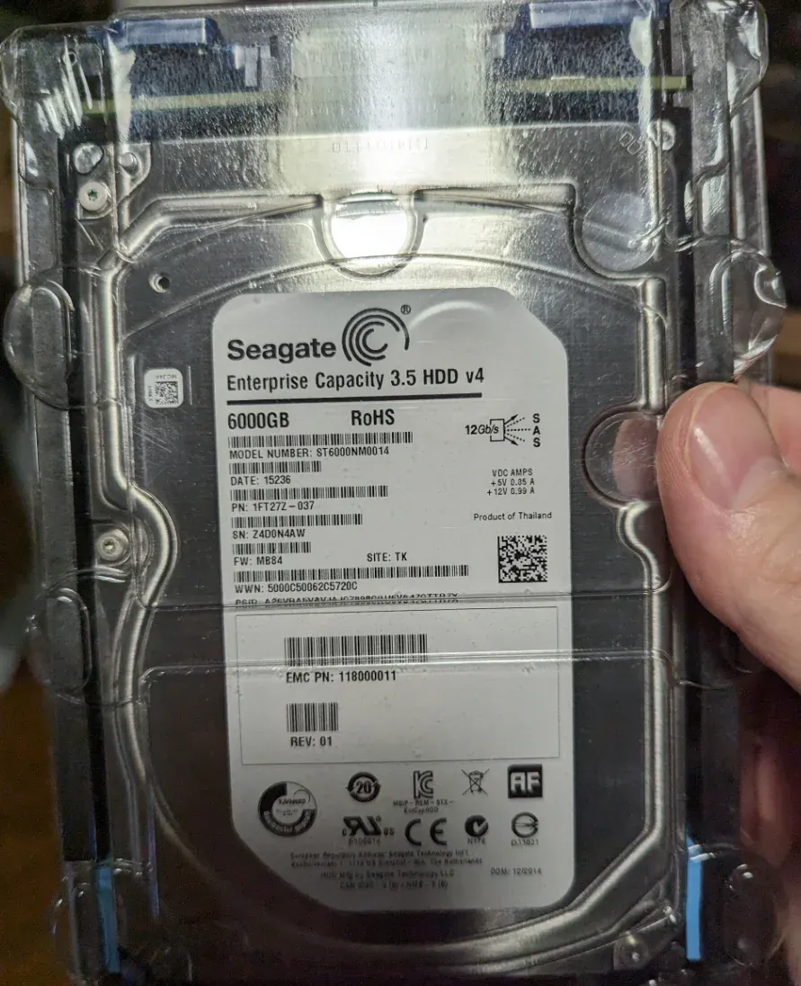 A brand new Seagate Enterprise SAS hard drive, still in the plastic shell. The label describes it as a Seagate 6000GB SAS Model ST6000NM0014.